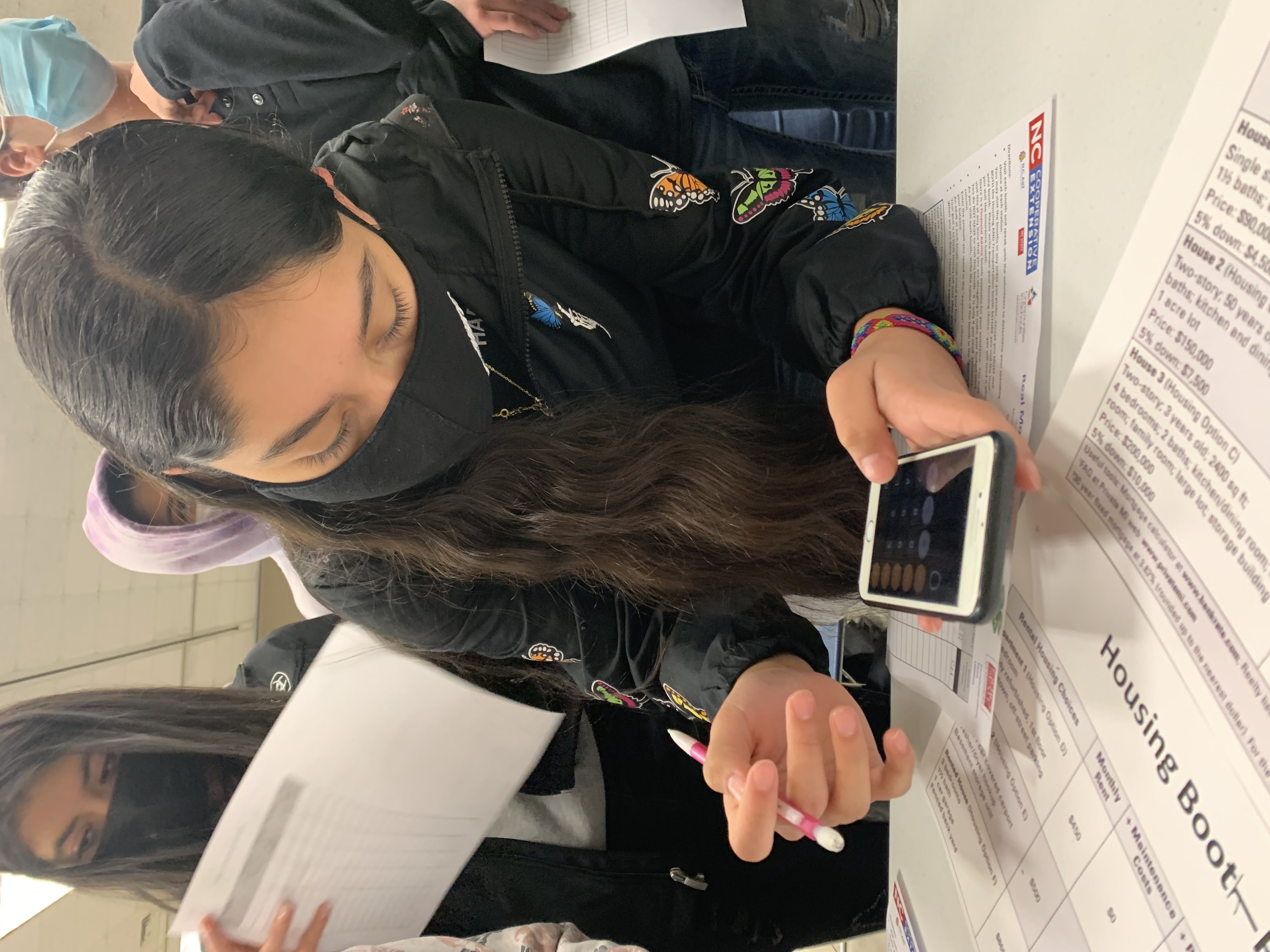 A girl doing a workbook using her phone's calculator.